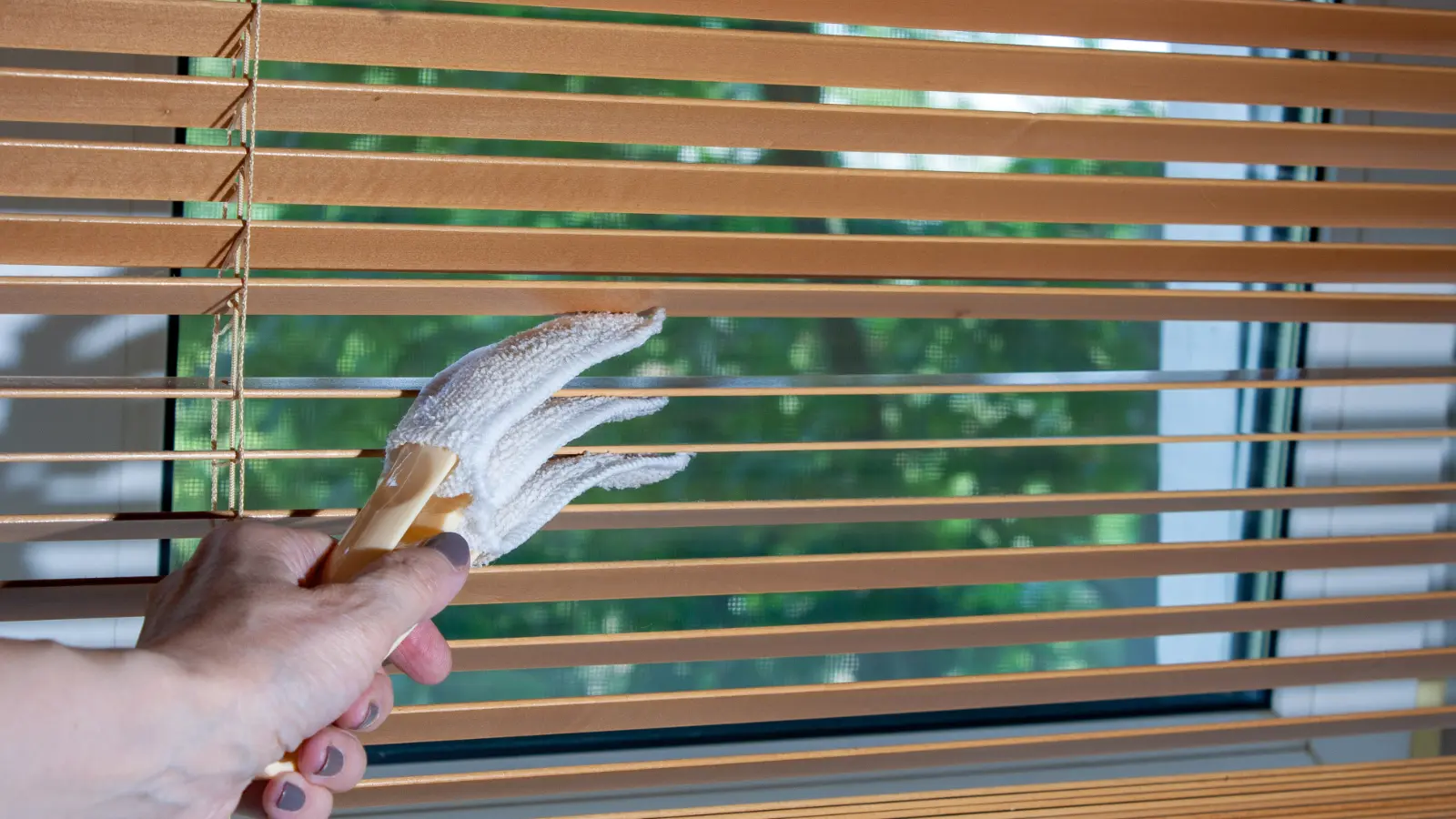 A person cleaning wooden blinds with a brush.
