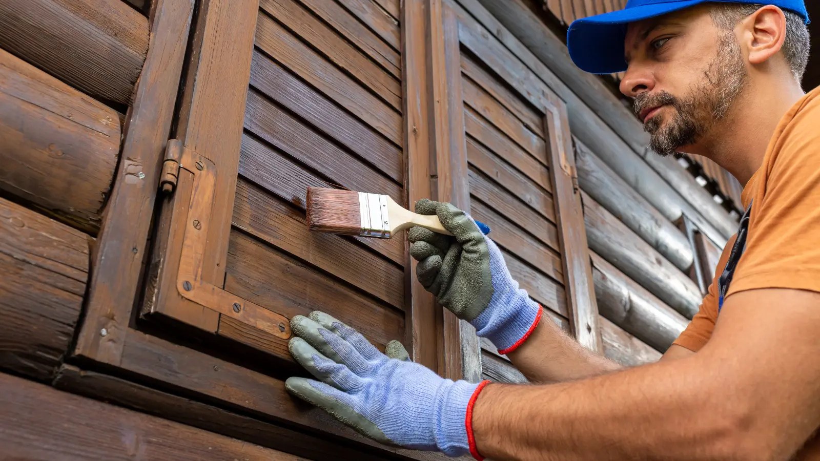 A man is painting the shutters of a wooden house.