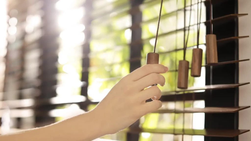 A person is holding a wooden blind in front of a window.