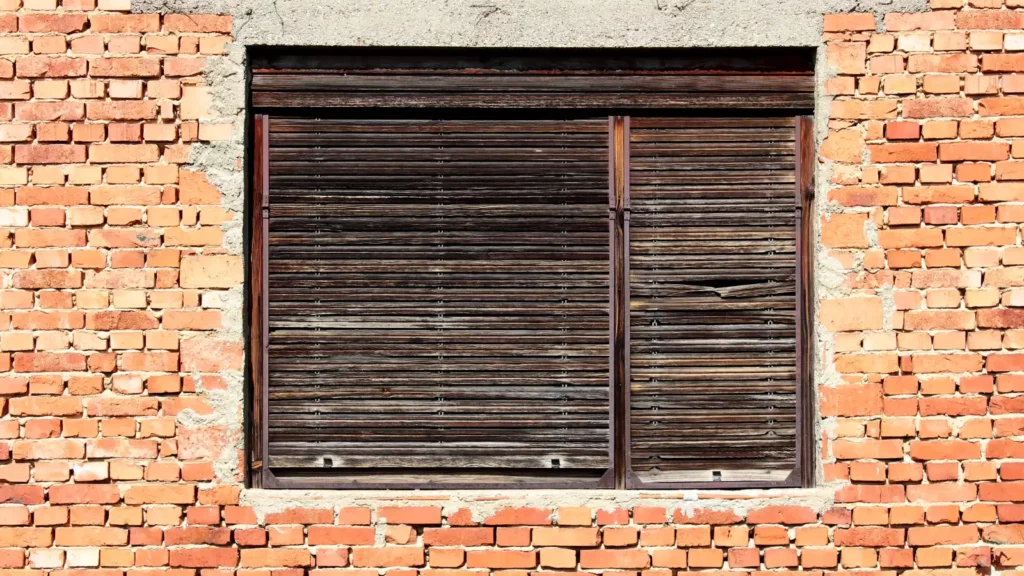 An old window with wooden shutters on a brick wall.