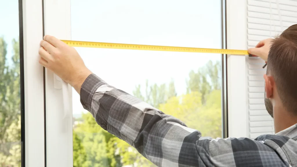 A man measuring a window with a tape measure.