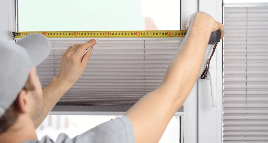 A man measuring the window blinds with a tape measure.