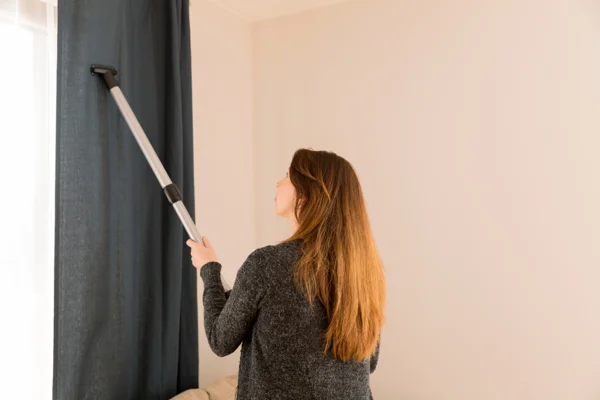 Cleaning drapes with a vacuum cleaner.