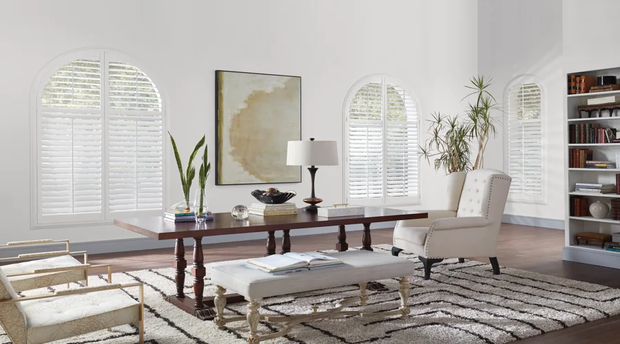 A living room with white shutters and bookshelves.