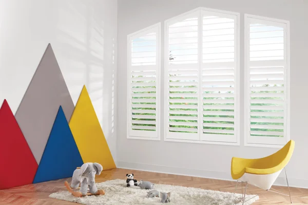 A child's room with white shutters and a colorful rug.