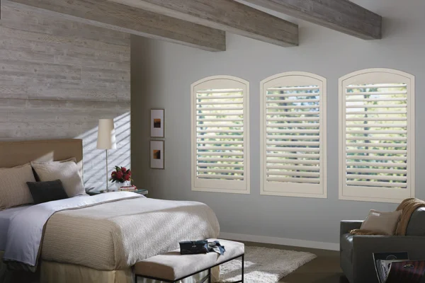 A bedroom with white shutters and a bed.