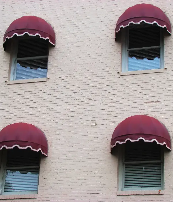 Four four maroon dome awnings on a white brick building.