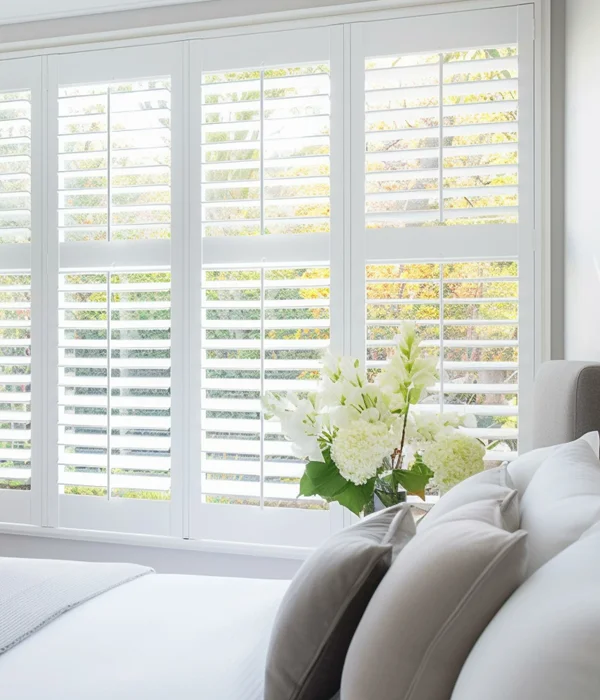 White shutters in a window with a view of the garden.