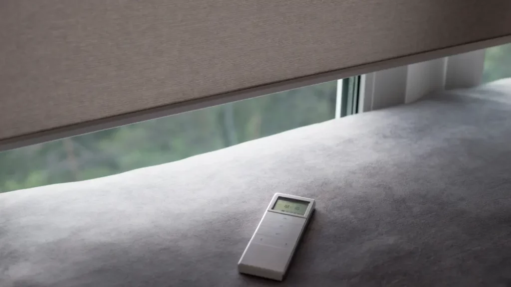 A remote control is sitting on a couch next to a window.