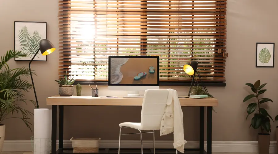 A home office with wooden blinds and a white desk.