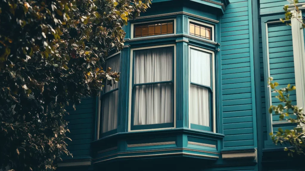 Teal Victorian bay window with white curtains