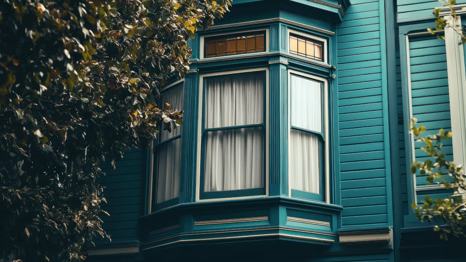 Teal Victorian bay window with white curtains